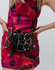 Person wearing a red and black patterned set with sunglasses around the waist on a plain background