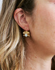 Close-up of a person wearing gold earrings with a central gemstone.