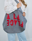 Person holding a striped bag with red letters against a white background