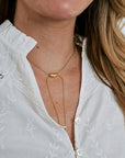 Close-up of a person wearing a gold necklace against a white blouse.