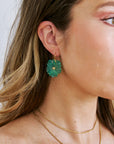 Close-up of a person wearing green floral earrings and a gold necklace.