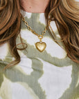 Close-up of a person wearing a gold necklace with a heart pendant