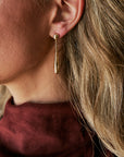 A close-up side profile of a woman wearing a delicate gold teardrop dangle earring