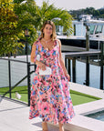 Woman in a floral dress standing by a waterfront with palm trees in the background