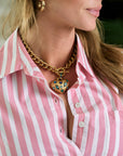 Woman wearing a pink and white striped shirt with a gold necklace featuring a heart pendant.