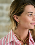 Woman wearing a pink striped shirt and gold jewelry outdoors