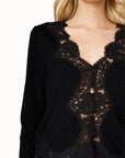 detail close up of a model wearing a black cardigan with lace trim and blue jeans on a white background