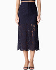 A model wearing a dark navy blue lace midi skirt with a scalloped hem, paired with a matching crop top and black sandals, shown against a plain white background.
