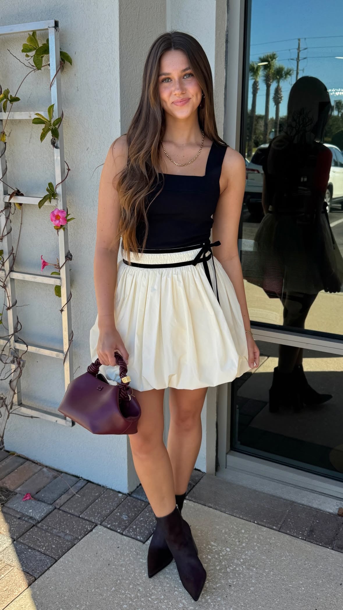 Woman in a black top and white skirt standing outside a building.