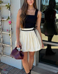 Woman in a black top and white skirt standing outside a building.