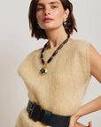 Woman wearing a beige sleeveless top with a black belt and a long necklace against a plain background