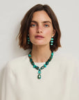 Woman wearing a green beaded necklace and earrings against a plain background