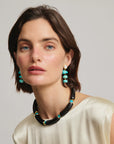 Woman wearing a black and turquoise beaded necklace and earrings against a neutral background