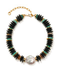 A beaded necklace featuring black disc-shaped beads, small turquoise green beads, gold spacer rings, and a large irregular white pearl at the bottom center, displayed on a clean white background.