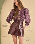 Model wearing a patterned blouse and leather skirt with text labels on a beige background