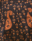 A close-up of a dark fabric with an orange paisley and floral block print pattern.