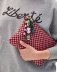Person holding a pink checkered clutch with Cameo Fob against a gray sweatshirt background.