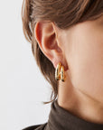 Gold hoop earrings worn by a person with a neutral background