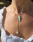 Necklace with a green pendant and pearl drop worn by a person in a white top.