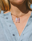 Close-up of a person wearing a necklace with fish-shaped pendants against a blurred outdoor background.
