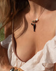 Close-up of a person wearing a white top and a necklace with a fish pendant.