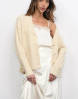 Woman wearing a cream cardigan over a white outfit against a plain background