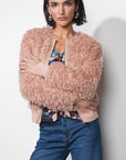 Woman wearing a fluffy pink jacket and blue jeans against a white background