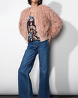 Woman wearing a fluffy pink jacket, floral top, and blue jeans against a white background