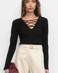 Woman wearing a black top with criss-cross design and beige pants against a white background