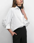 Woman wearing a white shirt and black pants against a plain background
