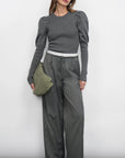 Woman wearing a gray outfit with wide-leg pants and a green bag against a white background