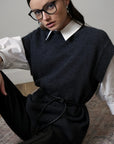 Woman wearing a dark sweater vest over a white shirt with a plain background