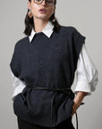 Woman wearing a dark gray sweater vest over a white shirt on a gray background