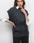 Woman wearing a dark gray knitted vest over a white shirt with a plain background, front view