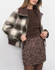 Woman wearing a plaid jacket, brown sweater, and leopard print skirt on a white background