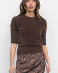 Woman wearing a brown knit sweater and leopard print skirt against a white background, front view