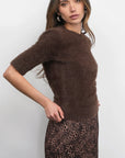 Woman wearing a brown sweater over a leopard print skirt on a white background, side view