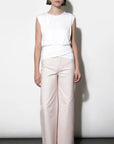 Woman wearing a white sleeveless top and light pink pants against a white background