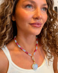 Woman wearing a beaded necklace with a heart pendant in front of a geometric patterned wall.