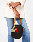 Person holding a black handbag with decorative charms against a white background