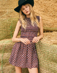 Woman in a patterned dress and black hat standing among hay bales.