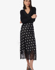 Woman wearing a black top and black polka dot skirt with lace trim on a white background