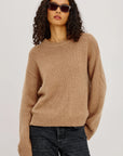 Woman wearing a brown sweater and sunglasses on a plain background