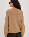 Person wearing a beige sweater and dark jeans on a plain background