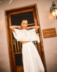 Woman in a white outfit standing in front of a wooden door with a sign on the wall.