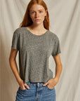 A woman with red hair wearing a heather gray short-sleeve crewneck t-shirt and blue jeans, standing against a draped beige fabric backdrop.
