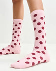 Pink socks with red polka dots worn by a person on a light gray background