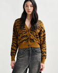 Woman wearing a mustard yellow cardigan with black tiger stripe pattern and gray jeans on a white background