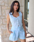 Woman wearing a light blue sleeveless top and shorts standing outdoors.