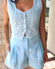 Woman wearing a light blue sleeveless top and shorts set with a textured wall background